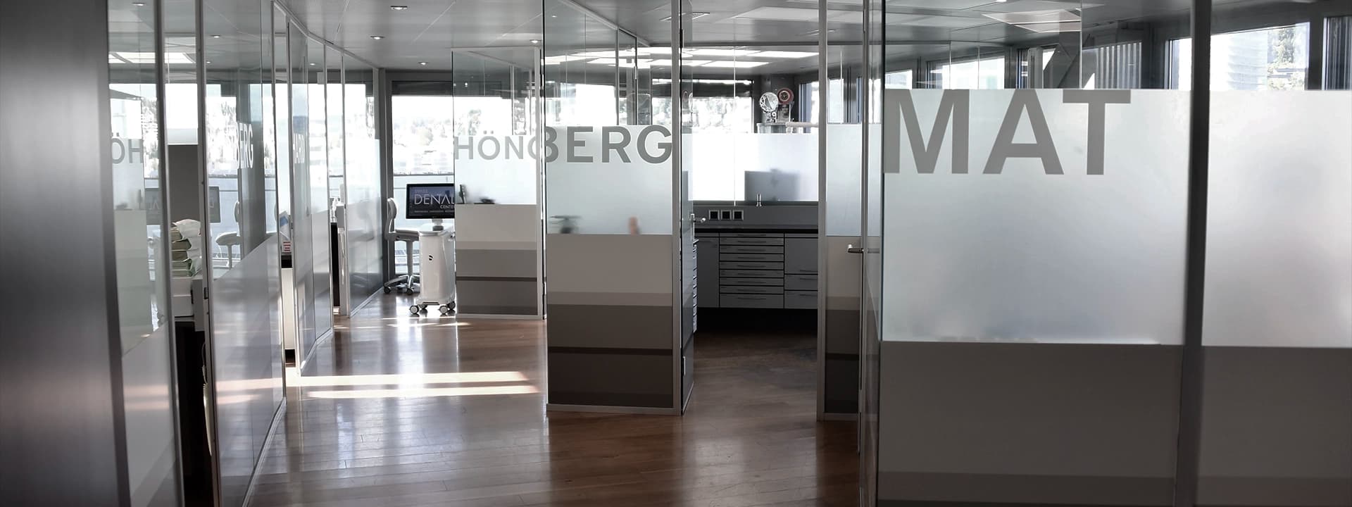 Praxisbereich des Swiss Dental Center mit modernen Glastrennwänden, beschrifteten Türen und hellen, klar strukturierten Behandlungszimmern.