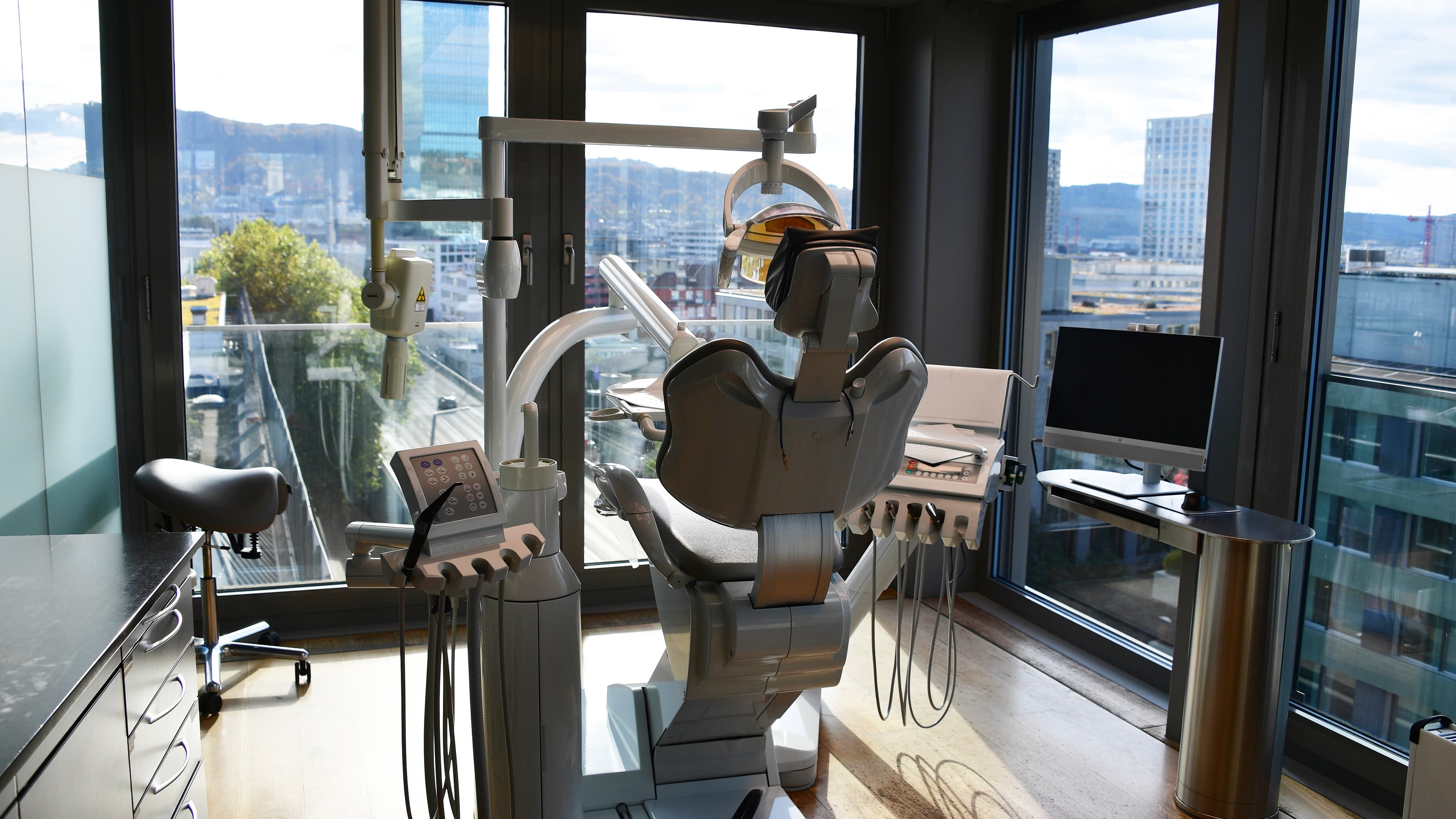 Moderner Behandlungsraum der Swiss Dental Center Praxis mit hochentwickeltem Zahnarztstuhl, zahnmedizinischen Geräten und großem Fenster mit Stadtblick.