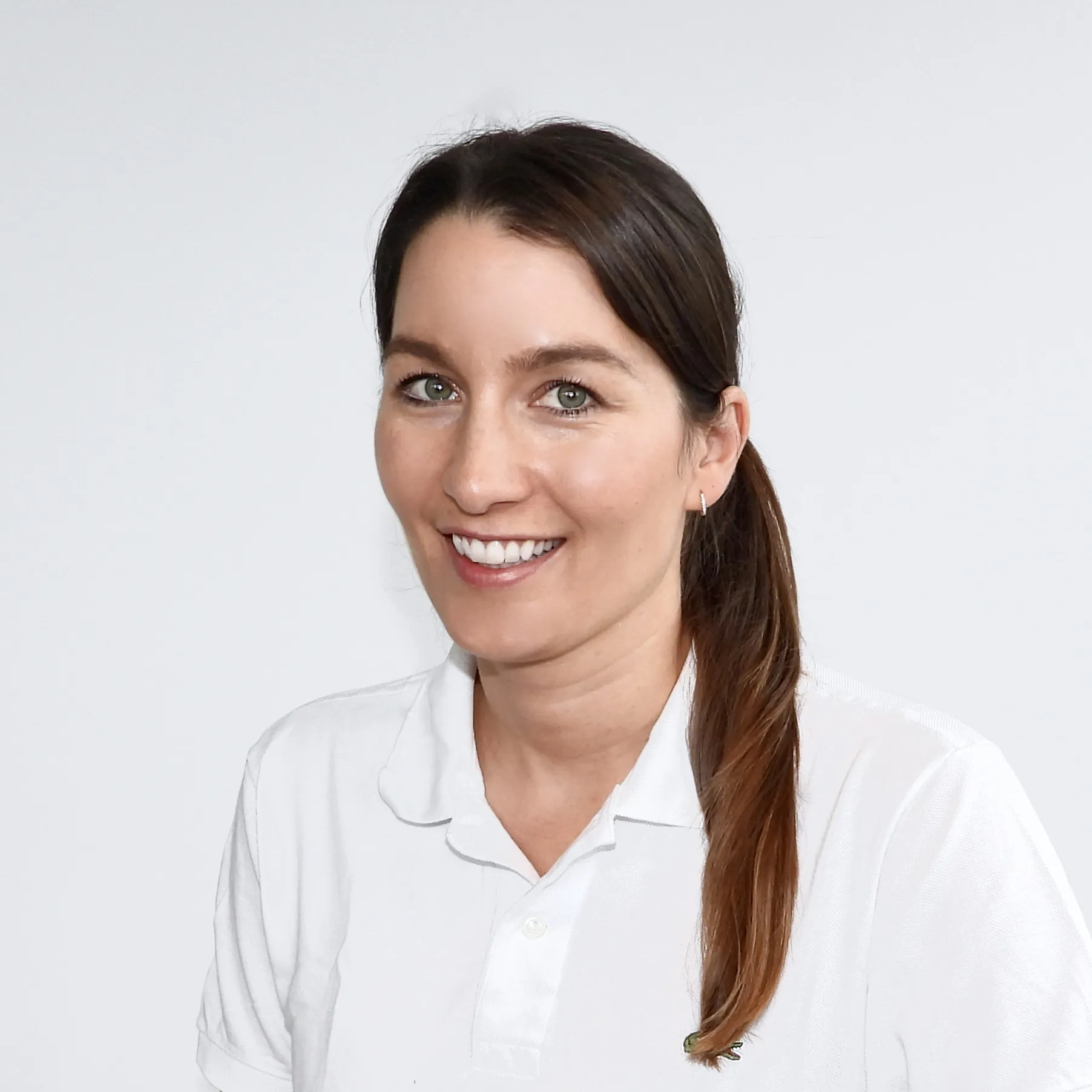 Sie lächelt freundlich, trägt ein weisses Oberteil und hat ihr dunkles Haar zu einem Pferdeschwanz gebunden.
