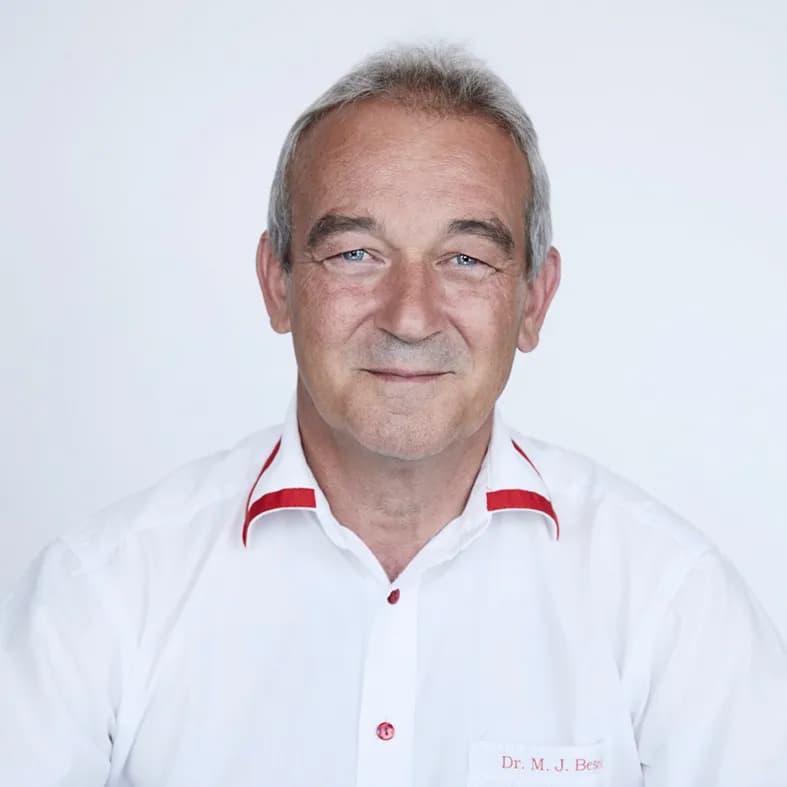 Er lächelt freundlich in die Kamera und trägt ein weisses Hemd mit roten Akzenten.